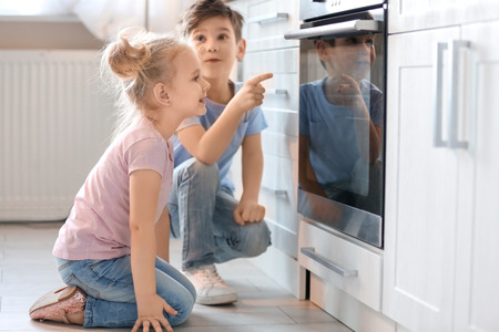 Little kids sitting near oven indoorsの写真素材