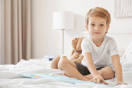 Cute boy reading book on bed at homeの写真素材