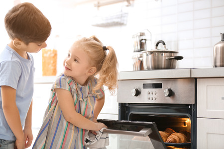 Little kids sneaking croissants from oven indoorsの写真素材