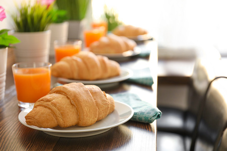 Plates with delicious croissants and glasses of juice on wooden table in cafe