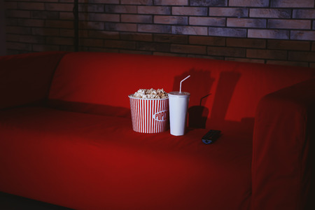 Comfortable couch with popcorn, drink and remote control indoors. Home cinemaの写真素材