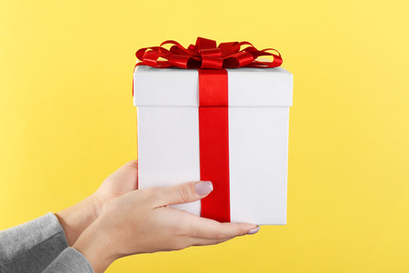 Woman holding gift box on color background