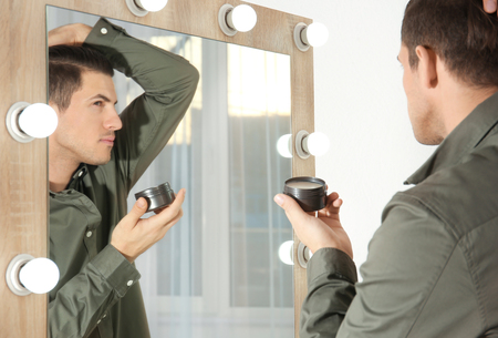 Handsome young man applying clay for hair near mirror at homeの写真素材