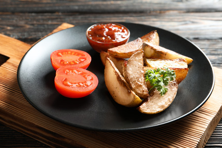 Plate with delicious baked potato wedges on wooden boardの写真素材