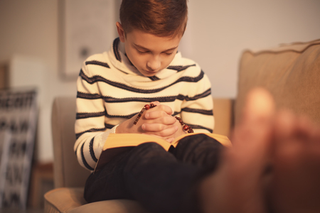 Little boy praying on sofa indoorsの写真素材