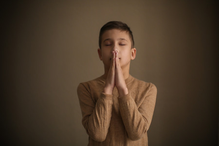 Little boy praying on dark backgroundの写真素材