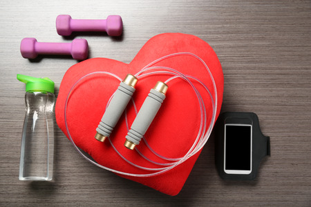 Gym stuff, phone and red heart on wooden background. Cardio training concept