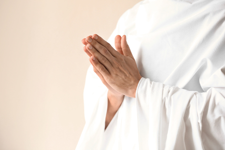 Young monk praying to God on light background
