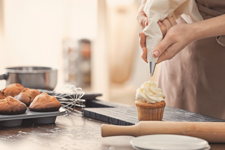 Woman decorating tasty cupcake with cream at tableの写真素材