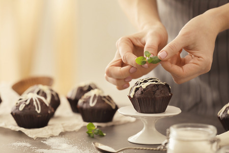 Woman decorating tasty cupcake with mint at tableの写真素材