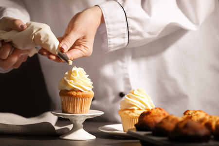 Chef decorating tasty cupcake with cream at tableの写真素材