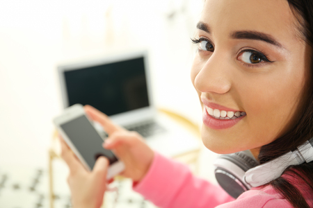Beautiful young woman with headphones and mobile phone at homeの写真素材