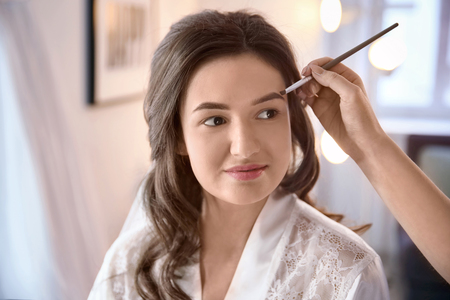 Makeup artist preparing bride before her wedding in roomの写真素材