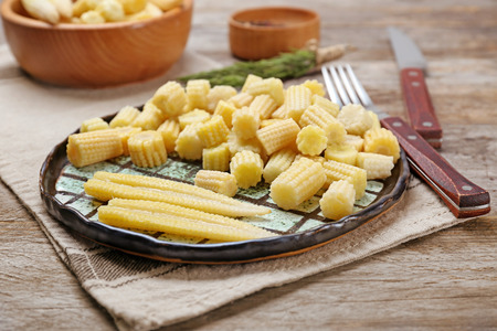 Plate with fresh young baby corn on wooden tableの写真素材