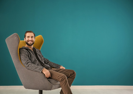 Handsome man sitting in comfortable armchair against color wallの写真素材