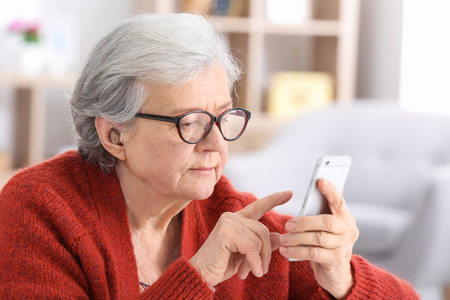 Mature woman with hearing aid using smartphone indoorsの写真素材