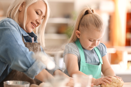 Little girl and her grandmother preparing dough together in kitchenの写真素材