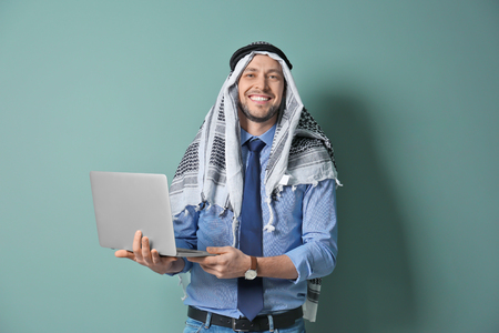 Muslim businessman in traditional clothes with laptop on color backgroundの写真素材