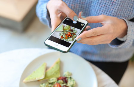 Young woman taking photo of delicious food with mobile phone at cafe, closeupの写真素材