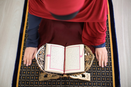 Young Muslim woman reading Koran, indoors