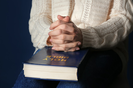 Religious young woman praying over Bible, closeup