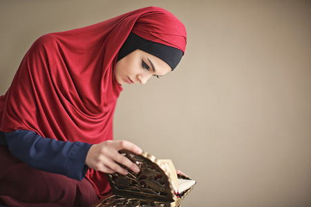 Young Muslim woman reading Koran on color backgroundの写真素材