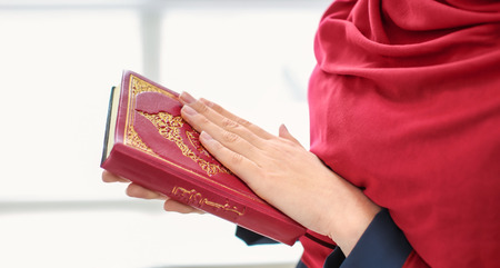 Young Muslim woman holding Koran and praying, indoorsの写真素材
