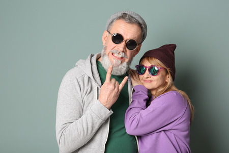 Happy senior couple in hipster outfits on grey background