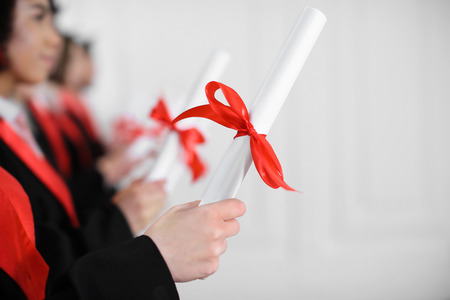 Students in bachelor robes with diplomas indoors. Graduation day
