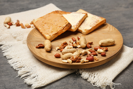 Wooden plate with toasted bread and nuts on table