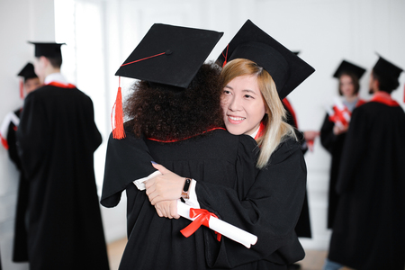 Happy students in bachelor robes hugging indoors, Graduation dayの写真素材