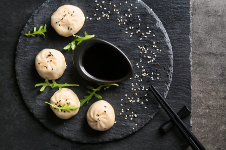 Slate plate with tasty baozi dumplings and soy sauce on tableの写真素材