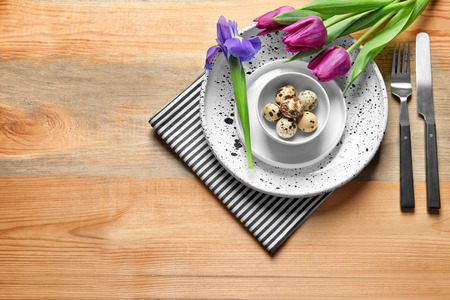 Beautiful festive Easter table setting with quail eggs and flowers on wooden background