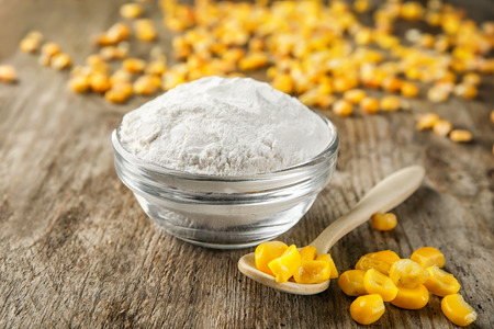 Spoon with kernels and corn starch in bowl on wooden table