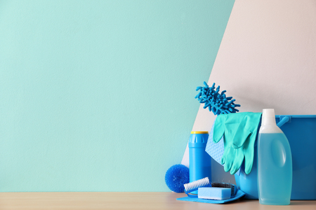 Bucket with cleaning supplies and tools on table near color wallの写真素材