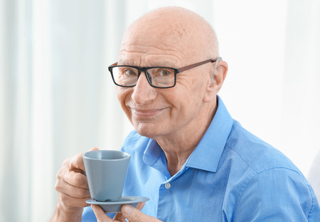 Senior man with hearing aid drinking tea indoorsの写真素材