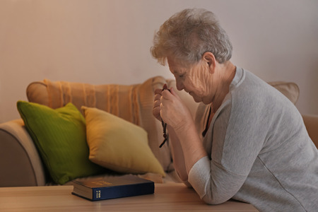 Religious elderly woman praying over Bible at tableの写真素材