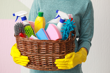 Woman holding basket with cleaning supplies on color backgroundの写真素材