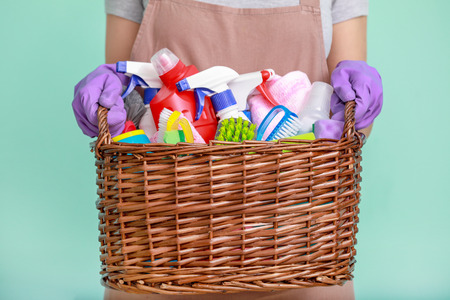 Woman holding basket with cleaning supplies on color backgroundの写真素材
