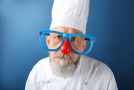 Mature man in chef uniform and funny glasses on color background. April fool's day celebrationの写真素材