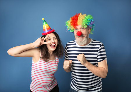 Young woman and mature man in funny disguise on color background. April fool's day celebrationの写真素材