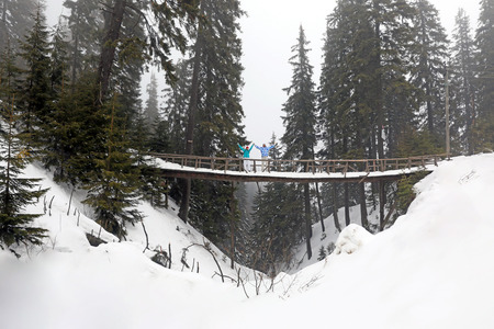 Happy couple standing on bridge in snowy forest. Winter vacationの写真素材