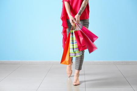 Beautiful young woman with shopping bags against color wallの写真素材