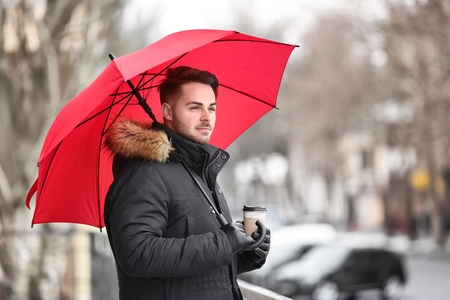 Young man in warm clothes with red umbrella outdoorsの写真素材