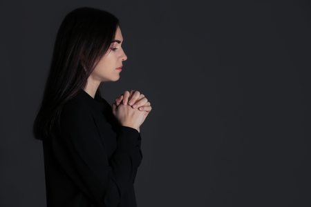 Religious young woman praying on dark backgroundの写真素材