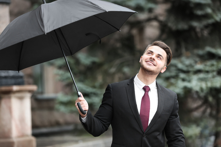 Young man in elegant suit with dark umbrella outdoorsの写真素材