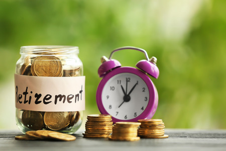 Coins in glass jar and alarm clock on blurred  background. Time for pension planningの写真素材