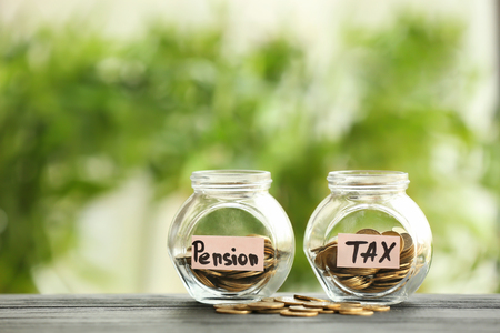 Glass jars with coins on table against blurred background. Pension planning conceptの写真素材