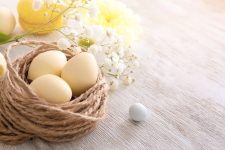 Decorative nest with chocolate Easter eggs and flowers on wooden background
