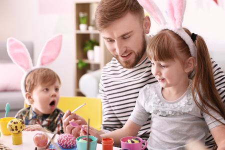 Father painting Easter eggs with his children at table